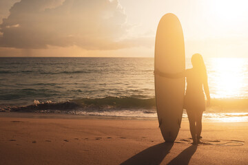 Fototapeta na wymiar Silhouette of surfer woman carrying their surfboards on sunset beach with sun light.