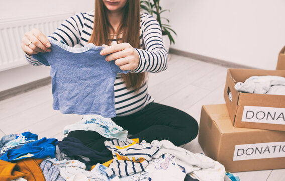 Pregnant woman is sorting baby clothes and wanna give some things to charity