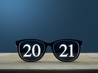 2021 white text with black eye glasses on wooden table over light blue gradient background, Business vision happy new year 2021 concept