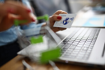 Credit bank card is holding small shopping basket next to laptop. Online shopping on the internet...