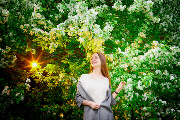 Outdoor portrait of a beautiful young girl near blossom apple trees with white flowers.