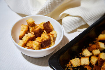 Square toasted pieces of homemade delicious rusk, hardtack, Dryasdust, zwieback on a white plate and baking sheet.