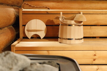 The wooden sauna accessories are in front of heater in steam room. Focus on the bucket.