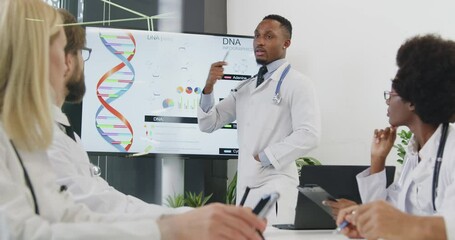 Group of attractive concentrated international doctors listening seminar on dna theme which holding experienced bearded black-skinned colleague