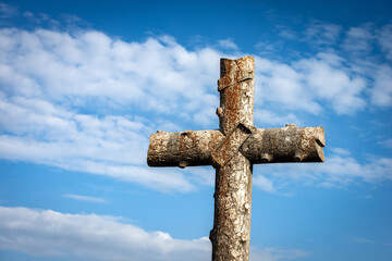 Ancient christian cross made of stone on blue sky with clouds (imitation of a tree trunk), near the...