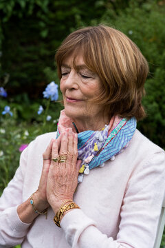 Woman with her hands together and eyes closed seated in a garden 