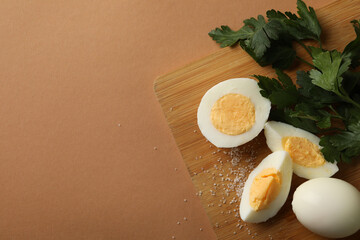 Board with boiled eggs, salt and parsley on brown background