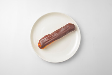 Milk chocolate eclair on plate on white background. Delicious vanilla dessert for tea time.