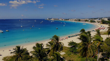 Aerial of the beautiful beach in Barbados. A view over palm trees on a beach, blue water and boats 