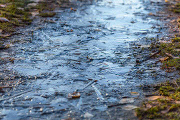 Frozen dirty puddle on the path in the morning after the first night frost. Close up