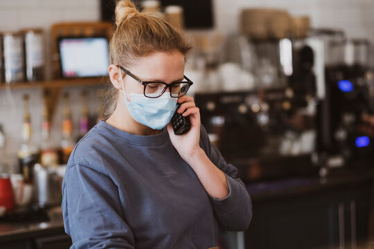 Blond waitress wearing face mask working in a cafe, on the phone.