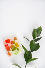 Soap with colorful pieces, green plant branch, white background. Hygiene, disinfection, natural product concept. Top view, flat lay, copy space, vertical format