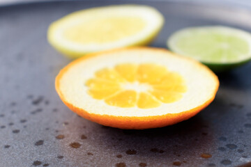 Plate with citrus fresh fruit tangerines with leaves, lemon, lime orange on a dark round plate on a concrete background . vitamins, close-up