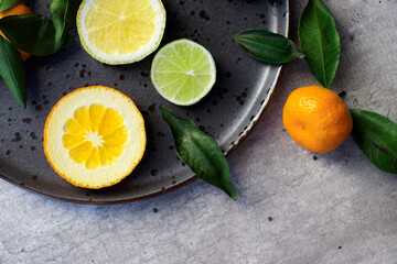 Fototapeta na wymiar Plate with citrus fresh fruit tangerines with leaves, lemon, lime orange on a dark round plate on a concrete background . vitamins, close-up