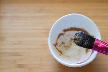 a jar and brush with a homemade clay face mask on a wooden table