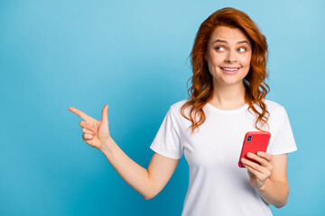 Photo portrait of dreamy woman pointing finger at blank space holding phone in one hand isolated on pastel blue colored background