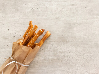 grissini breadsticks with sesame seeds in a paper bag with a bow on a light background with a checkered towel with space for text top view
