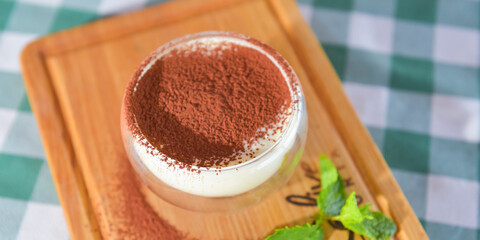 Tiramisu cake served in a glass over blurred restaurant background. Italian cuisine concept.