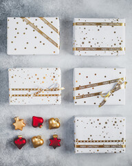 Gift boxes in white paper with stars and dots with golden ribbons on grey background. Christmas and New Year background. 