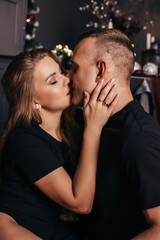 View of a passionate romantic couple spending time before New Year at home with garlands. Young woman and handsome man hug, kiss. Christmas time.