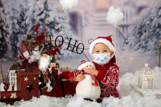 Cute boy, toddler child, having his christmas pictures taken playing in the snow outdoors, wearing protective mask