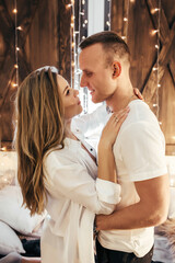 Romantic couple spending time before New Year at home with garlands. Young woman and handsome man hug, kiss. Christmas time. Happy couple in new year