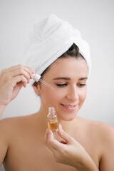 Portrait of beautiful young woman with towel on head holding face oil.