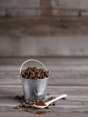 Arabica coffee beans in a small miniature bucket. ground coffee in a white ceramic spoon on a wooden background