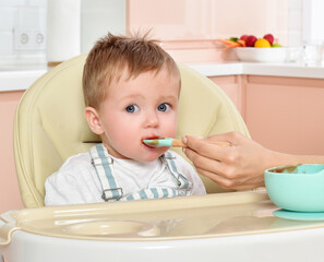 Young mother spoon-feeds the child. Feeding baby. Baby food.