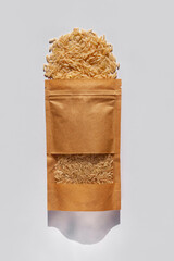 Kraft paper pouch bag with whole grain brown rice top view with harsh shadow on white background. Healthy diet food packaging mockup flat lay. Dry uncooked thai cereal high fiber magnesium antioxidant