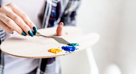 Close up of woman artist hands mixing colors on wooden art palette