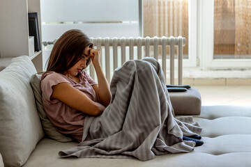 Obraz premium Young woman looking depressed, sitting on couch at home. Unhappy female feels lonely, thinking about problem sitting on couch at home. Lonely sad woman deep in thoughts sitting daydreaming. Copy space