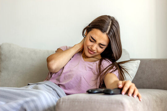 Young woman experiencing neck pain at home. Photo of woman sitting in bed and suffering from neck ache at home. Cropped shot of an attractive young girl suffering from neck ache while sitting at home.