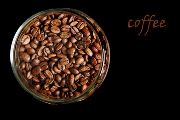 top view of black Arabica coffee beans in a round glass jar on a black background and the...