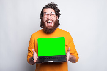 An excited man is looking at the camera and is holding a computer .