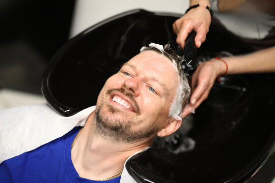 Portrait of smiling man who is being washed with shampoo in salon by master. List of services in beauty salons and hairdressing salons concept