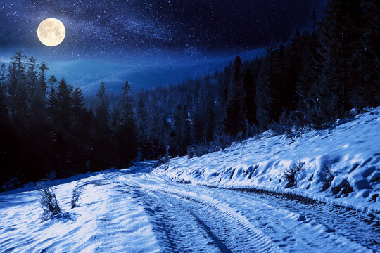 carpathian countryside on a winter night. beautiful mountainous rural landscape in full moon light. road through snow covered meadow among spruce forest on the hill