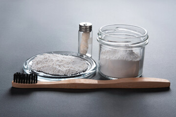 Zero waste concept for teeth cleaning. A bamboo toothbrush with a floss in a glass and toothpowder on the grey background.