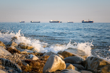 Stone seashore, waves and cargo ships waiting in line to enter the port at the background