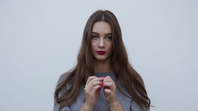 A young, frightened woman stands against the background of a gray wall, wringing and squeezing her hands, expressing intense concern. Young woman in a state of depression .High quality FullHD footage