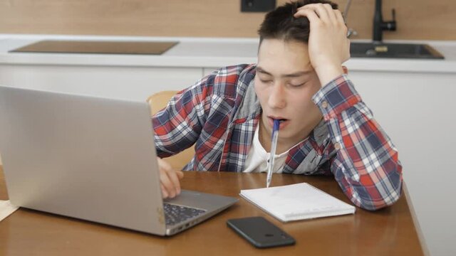Bored lazy young student working on laptop computer and with paper documents. Tired young business man sleeping above documents. Focused guy student distance learning at home office, kitchen