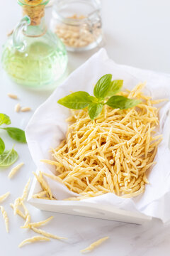 Fresh homemade short twisted pasta Trofie - typical of Liguria Region in Italy - with basil, olive oil and pine nuts at the background