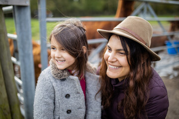 Fototapeta premium Smiling mother and daughter looking at the distance with alpacas behind them
