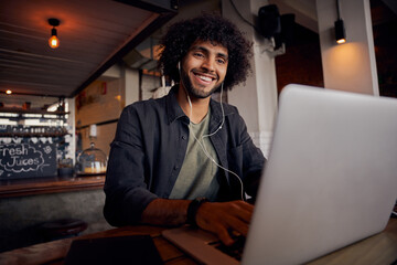 Happy young man watching video online on laptop with earphone in cafe