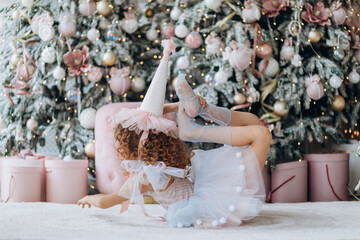 Beautiful Christmas decor in pink in the children's room. Girl playing near the Christmas tree - 391482600