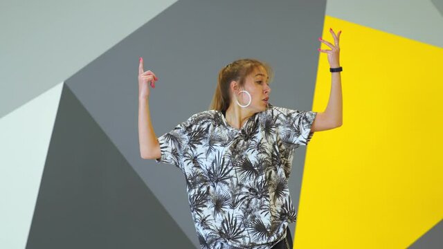 Beautiful woman dancing hip hop in the studio in front of the wall with bright geometric pattern. Medium long shot