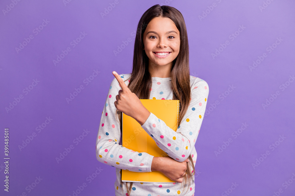 Wall mural Photo portrait of happy schoolgirl keeping copybook showing at empty space isolated on vivid purple color background