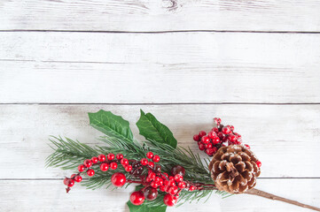 Christmas decorations made of spruce branches with red berries and brown natural pine cones on a light wooden background. Space for text, top view, flat lay. Branch from the bottom