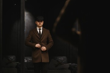 A man posing in the image of an English retro gangster of the 1920s dressed in a coat, suit and...