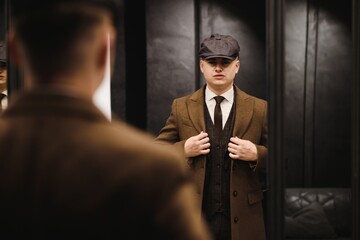 A man posing in the image of an English retro gangster of the 1920s dressed in a coat, suit and...